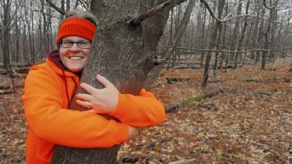 Sara Fitzsimmons hugs an American chestnut tree found growing in the wild near the orchard she helped plant. This tree is about 40 feet tall and is producing nuts but shows signs of chestnut blight.