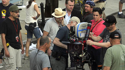 A camera near director Christopher Nolan, center in suit coat, and prdoucer Emma Thomas (in pink) is prepped for a scene.