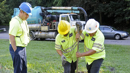 Shawn Mahoney (center) and Bob Scott (right) of Pittsburgh Water and Sewer Authority (PWSA) contractor Jet Jack Inc. muscle the heavy casing top back in position over a manhole along Washington Blvd. Monday morning. Eric Taper of the PWSA is at left. The casing an lid were knocked out of place by the raging storm water runoff during Friday's flash flood in the area.