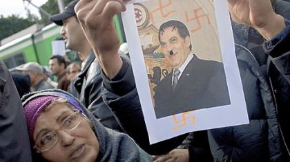 A woman views an image of former Tunisian president Zine El Abidine Ben Ali in which he is caricatured as Hitler during a demonstration against the Constitutional Democratic Rally party of the deposed president, in the center of Tunis Wednesday. A Tunisian prosecutor opened an investigation into the overseas assets of the ousted president and his deeply resented family Wednesday, as the United Nations said more than 100 people have died during five weeks of unrest.