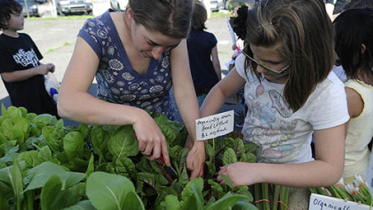 Farmer Gillian Goldberg, left, helps Zoe Moran, 11, of Arlington, pick out a Swiss chard plant at the Who Cooks for You Farm stand on the opening day of the CitiParks Farmers' Market in East Liberty.