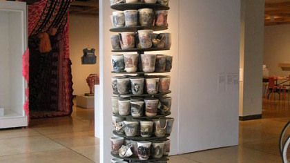 Ehren Tool "CBU 87" is made up of 14 shelves each holding 14 ceramic cups embellished with military and patriotic imagery, contained within the suspended shape of a large bomb.