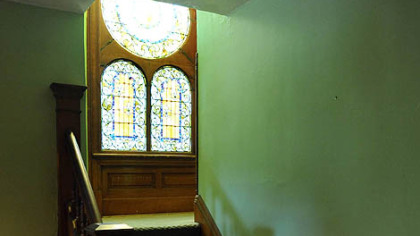 The staircase of the Victorian home leads to a landing dominated by three stained-glass windows.