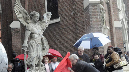 The rain pours down as sculptor James Simon, far left, and Paul Sciullo, center, unwrap Mr. Simon's sculpture of St. Michael. The unveiling followed a memorial Mass at St. Joseph Church in Bloomfield for the three slain police officers.