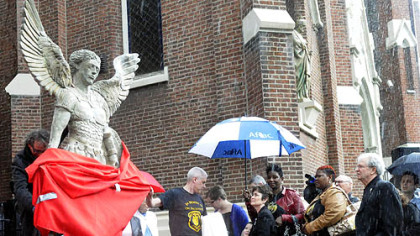 Artist James Simon, left, unwraps his sculpture of St. Michael as a memorial to three slain Pittsburgh police officers following a memorial Mass at St. Joseph Church, Bloomfield.