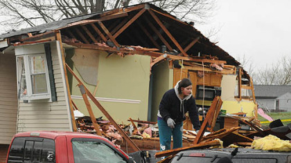 Brittany Zimmerman picks lumber from her father's truck while a neighbor's home sits in the background with the living room and kitchen exposed along Fosterville Road in Hempfield on Thursday.