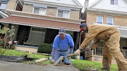 Volunteers Dave Majcher, left, and Clarence Swindle finish putting in replacement concrete outside a home in the 7400 block of Race Street in Pittsburgh's Homewood neighborhood. Volunteers and the Redd Up Pittsburgh cleanup crew took on the task of cleaning up several blocks of the street Thursday.