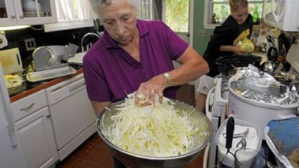 Freda Vogelsberger mixes in the salt. Three tablespoons of canning salt to 5 pounds of cabbage is a good ratio.   Dana Tabay, of New Brighton, cuts cabbage in the background.