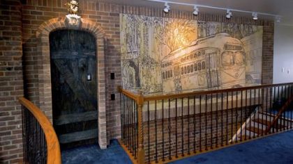 The third floor bedroom. Center, a faux doorway made of wood. On the door is a plaque labeled "610 3/4." To the right of the doorway is a mural, created by Joshua and Aaron Parise, featuring a streetcar.