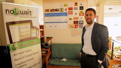 Luke Panza stands near one of the promotional  posters for No Wait, a company whose technologh helps local restaurants reach waiting customers. They presented at the 3 Rivers Venture Fair.