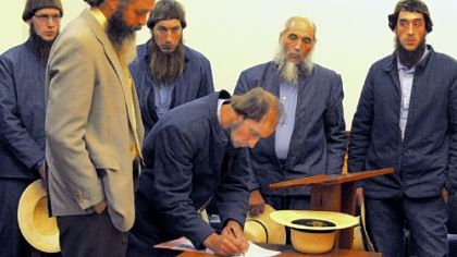 In a file photo, Johnny Mullet signs documents during a preliminary hearing in October in the Holmes County Courthouse in Millersburg, Ohio. In the foreground is his attorney, Andy Hyde, and behind him, from left to right, are Lester Mullet, Daniel Mullet, Levi Miller and Eli Miller.
