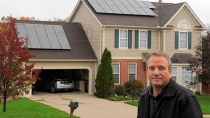 George Totolos stands across the street in front of his Cranberry home equipped with solar panels. Mr. Totolos said the voltage he gets from his panels will convert to 20,000 miles of driving his Chevy Volt.